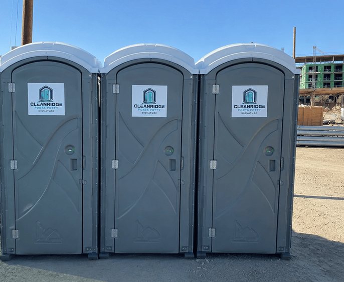 Three Cleanridge portable toilets lined up along the edge of a construction site