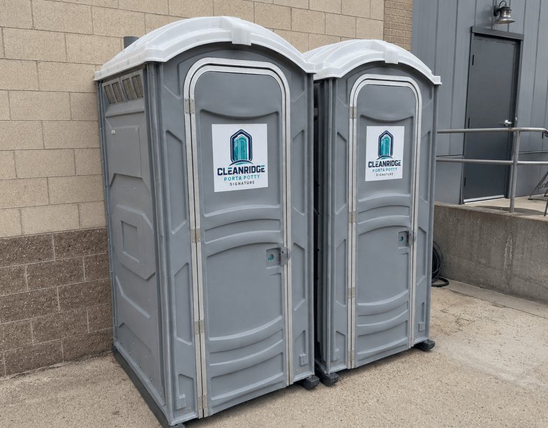 Pair of Cleanridge portable toilets placed against a block wall on a jobsite